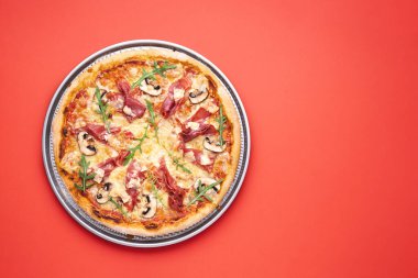 Pizza üstü, ev yapımı prosciutto, roka, şampiyonlar ve mozzarella. Lezzetli jambonlu pizza. Kırmızı masada pizzayla manzaranın üstünde.