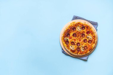 Pizza taşında lezzetli pepperonili pizza, fırın tazeliğinde, dikişsiz mavi bir arka planda. Pizza yemeye hazır bir şekilde yatıyordu. Otantik İtalyan yemekleri.