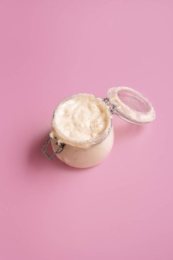 Pembe, pürüzsüz bir arka planda cam kavanozda mayalanmış mayalı ekmek. Ekmek yapmak için bir kavanoz kendi ellerimle yaptım. Anne hamuru buğday unundan.