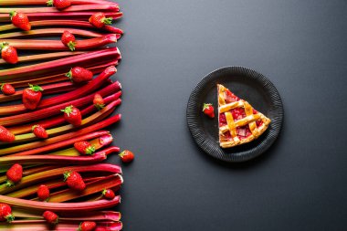 Rhubarb ve çilekli kek dilimi. Siyah tabakta tek dilim kafes kabuklu turta ve çiğ sebzeler ve meyveler.