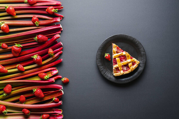 Rhubarb and strawberries slice of cake. Single slice of lattice crust pie in a black plate and the raw vegetables and fruits