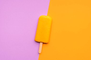 Çubukta vejetaryen portakallı dondurma, dikişsiz duotone arka plan. Mor arka planda portakallı buzlu dondurma. Yaz tatlısının düzlüğü..