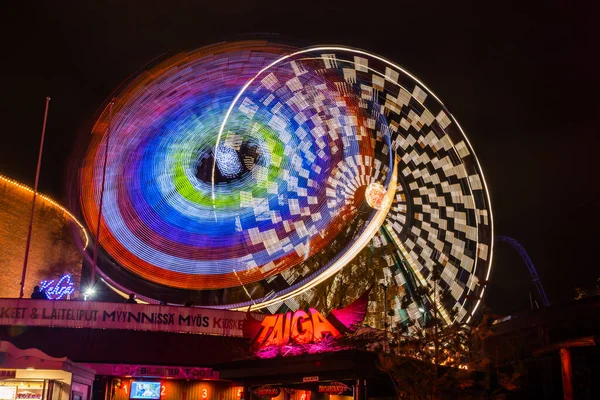 Helsinki, Finland - 19 October 2019: The Carnival of Light event at the Linnanmaki amusement park. Ride Ferris Wheel Rinkeli and Kehra in motion, night illumination, long exposure. — ストック写真