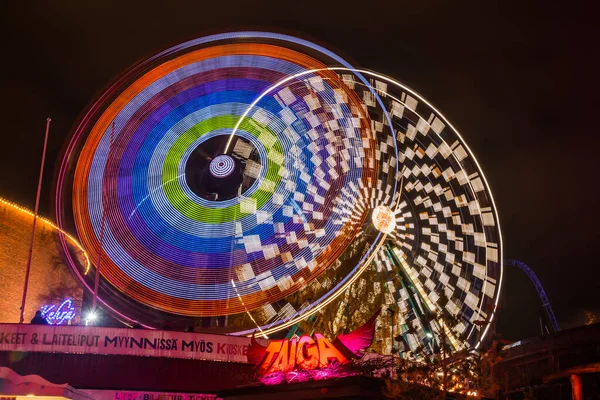 Helsinki, Finland - 19 October 2019: The Carnival of Light event at the Linnanmaki amusement park. Ride Ferris Wheel Rinkeli and Kehra in motion, night illumination, long exposure. — ストック写真