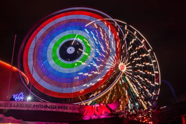 Helsinki, Finlândia - 19 de outubro de 2019: O Carnaval da Luz no parque de diversões Linnanmaki. Passeio Ferris Wheel Rinkeli e Kehra em movimento, iluminação noturna, exposição longa . — Fotografia de Stock