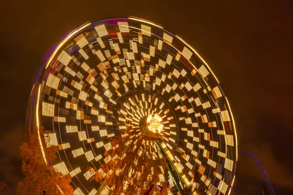 Rueda de la fortuna en movimiento en el parque de atracciones, iluminación nocturna. Larga exposición . —  Fotos de Stock