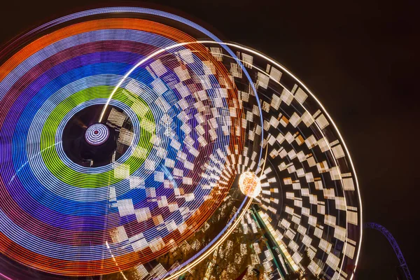 Two rides in motion in amusement park, night illumination. Long exposure. — Stock Photo, Image