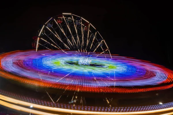 Two rides in motion in amusement park, night illumination. Long exposure. — Stock Photo, Image