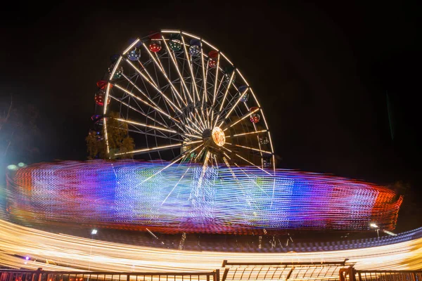 Due giostre in movimento nel parco divertimenti, illuminazione notturna. Lunga esposizione . — Foto Stock