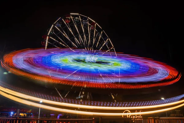 Dois passeios em movimento no parque de diversões, iluminação nocturna. Exposição longa . — Fotografia de Stock
