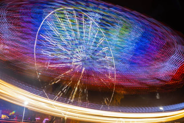 Dois passeios em movimento no parque de diversões, iluminação nocturna. Exposição longa . — Fotografia de Stock