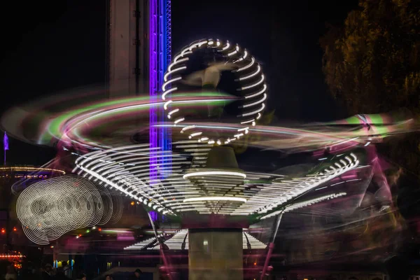 Um carrossel colorido desfocado em movimento no parque de diversões, iluminação noturna. Exposição longa . — Fotografia de Stock