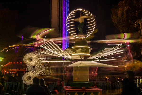 Una giostra sfocata colorata in movimento al parco divertimenti, illuminazione notturna. Lunga esposizione . — Foto Stock