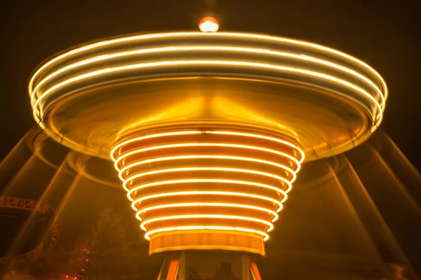 Un carusel colorat înceţoşat în mişcare în parcul de distracţii, iluminare nocturnă. Expunere lungă . — Fotografie, imagine de stoc