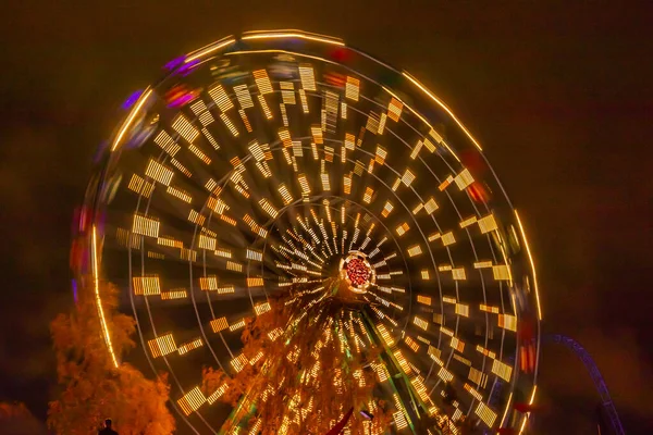 Ruota panoramica in movimento al parco divertimenti, illuminazione notturna. Lunga esposizione . — Foto Stock