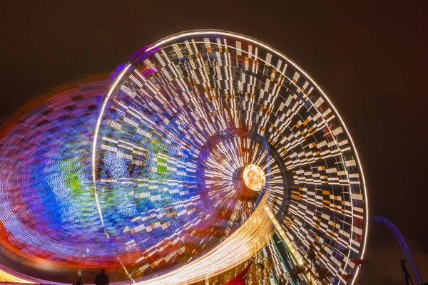 Two rides in motion in amusement park, night illumination. Long exposure. — Stock Photo, Image