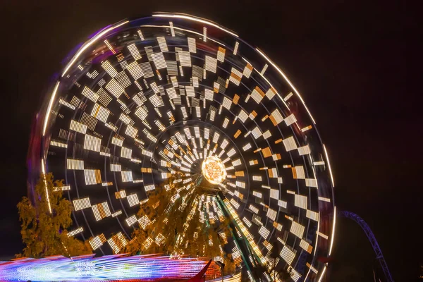 Two rides in motion in amusement park, night illumination. Long exposure. — ストック写真
