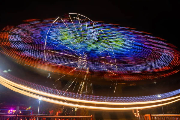 Two rides in motion in amusement park, night illumination. Long exposure.