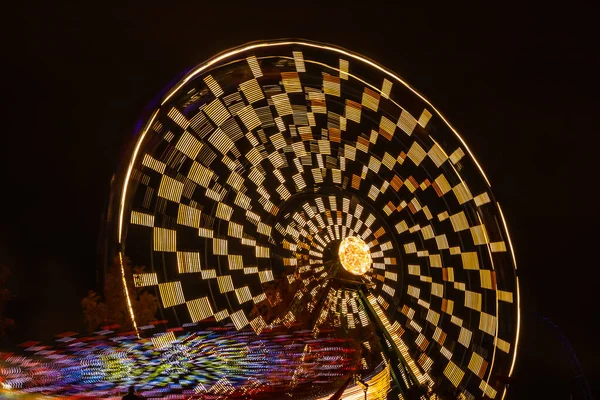 Two rides in motion in amusement park, night illumination. Long exposure. — Stock Photo, Image