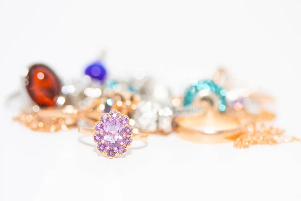 Коллекция ювелирных изделий с красивым золотым кольцом с фиолетовым камнем на белом фоне — стоковое фото