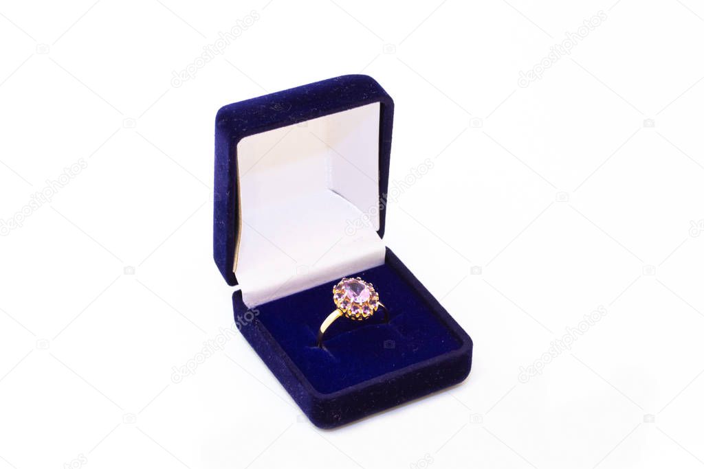 Golden ring with purple gemstone in a blue jewelry box on white background