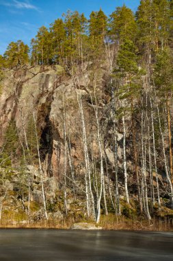 Finlandiya 'nın başkenti Repovesi' deki buzlu gölün üzerinde mağarası ve ağaçları olan yüksek kayalar.,