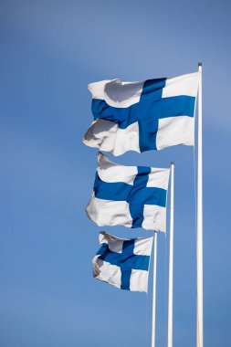 Mavi gökyüzüne karşı rüzgarda üç finnish ulusal bayrağı