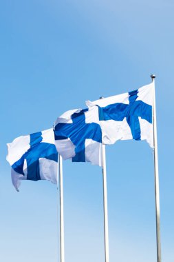 Mavi gökyüzüne karşı rüzgarda üç finnish ulusal bayrağı
