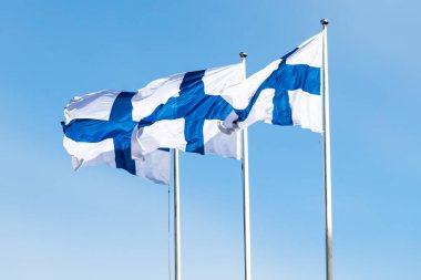 Mavi gökyüzüne karşı rüzgarda üç finnish ulusal bayrağı