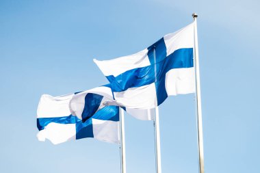 Mavi gökyüzüne karşı rüzgarda üç finnish ulusal bayrağı