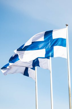 Mavi gökyüzüne karşı rüzgarda üç finnish ulusal bayrağı