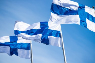 Mavi gökyüzüne karşı rüzgarda üç finnish ulusal bayrağı