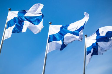 Mavi gökyüzüne karşı rüzgarda üç finnish ulusal bayrağı