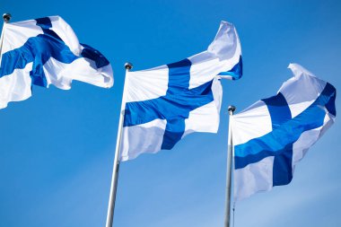 Mavi gökyüzüne karşı rüzgarda üç finnish ulusal bayrağı
