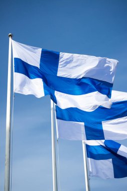 Mavi gökyüzüne karşı rüzgarda üç finnish ulusal bayrağı