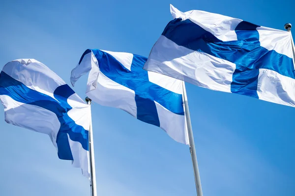 Mavi gökyüzüne karşı rüzgarda üç finnish ulusal bayrağı