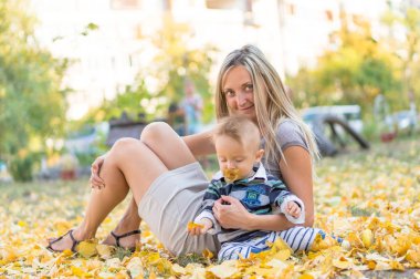 Mutlu anne ve küçük sarı ile oynarken oğlu gülümseyen parkta bırakır. Sonbahar.