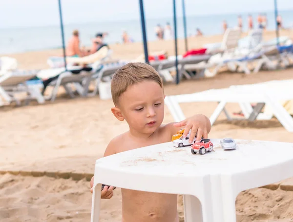 Junge sitzt am Strand und spielt mit Spielzeugautos. — Stockfoto