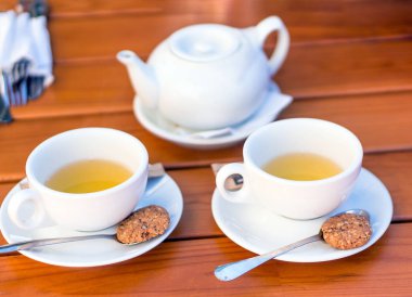 İki bardak çay ve bisküvi, kaşıklarla çaydanlık ahşap bir masa üzerinde beyaz