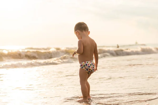 Lächelnder kleiner Junge, der bei Sonnenuntergang im Meer plantscht. — Stockfoto