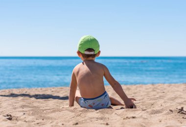 Oturma ve kumla oynayan küçük oğlu gülümseyen