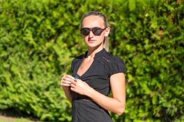 Çekici genç gülümseyen güzel kıvırcık sarı saçlı kız moda portre uzak sakin ara, arka plan yeşil çim çayırda arama poz içinde ince. Sağlıklı kadın yaşam tarzı kavramı. Siyah güneş gözlüğü.