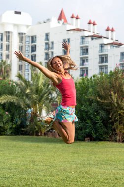 Çekici genç gülümseyen güzel kıvırcık sarı saçlı kız moda portre pembe tişört alan yaz yeşil çimen mavi gökyüzünde atlama içinde ince