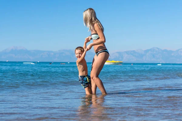 Joven madre e hijo niño sonriente jugando en la playa durante el día. Emociones humanas positivas, sentimientos, alegría . — Foto de Stock