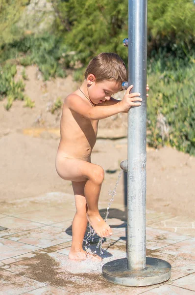 Kum ve tuz yıkamak için gün sahilde geçirdikten sonra onun Ayakkabı ve bir tatil beldesi, taze su jeti ile ayak kapalı hosing küçük çocuk