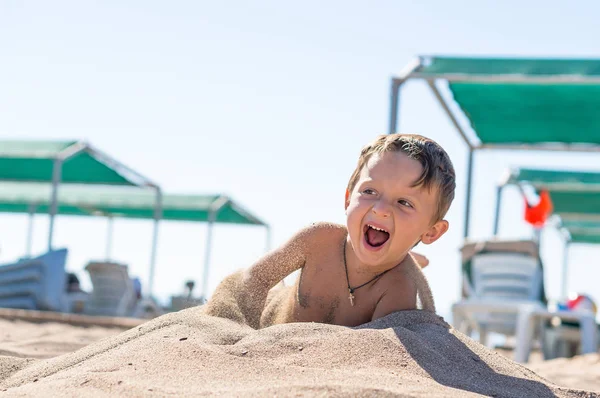 Lächelnder kleiner Junge, der sitzt und mit dem Sand spielt. positive menschliche Emotionen, Gefühle, Freude. — Stockfoto