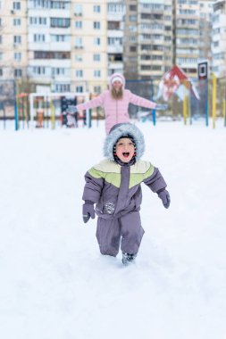 güzel gülümseyen yürümeye başlayan çocuk ve annesi karlı parkta eğleniyor. Etkin kış oyunu. Mutlu bir aile.