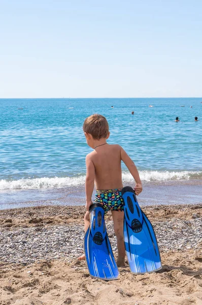 Entzückender kleiner blonder Junge, der Spaß am tropischen Strand hat. aufgeregtes Kind, das im Urlaub im sonnengeschützten Badeanzug im Meer spielt und surft. weißer Sand, Kind hält Schwimmflossen zum Schwimmen — Stockfoto