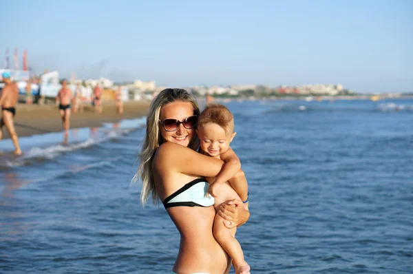 Joven madre y niño sonriente hijo jugando en la playa durante el día —  Fotos de Stock