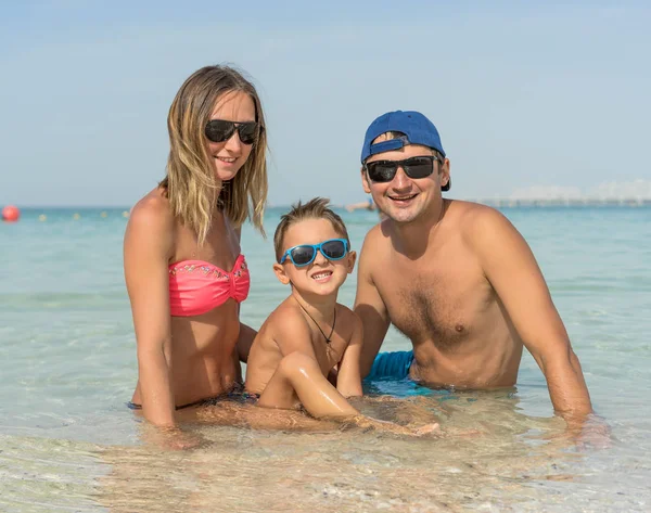 Mutlu bir aile tropikal beyaz kumsalda eğleniyor. Anne, baba, sevimli bir oğlan. Olumlu insan duyguları, duygular, joy. Tatil yapma ve yaz zevk komik şirin çocuk. Bahar ve yaz tatil.